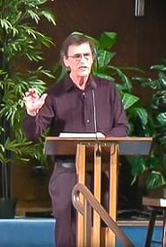Warren B. Smith standing in pulpit in front of green plants